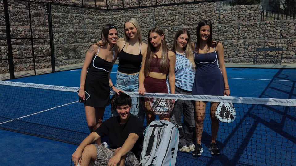 Un grupo de jugadoras y un jugador apoyados en la red de una cancha de pádel azul