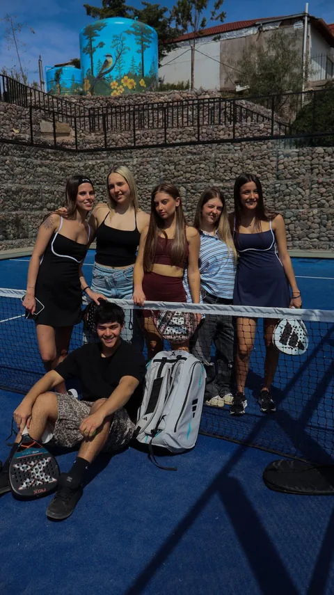 El mismo grupo en la cancha de pádel, con paletas y bolsos, en una foto vertical